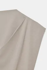 Top de algodón color beige, con cuello recto, mangas asimétricas y detalle de tejido drapeado en el lateral.