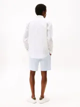 Camisa de lino blanco de manga larga con cuello clásico y cierre frontal de botones. Presenta un pequeño logo bordado de Tommy Hilfiger en el pecho.