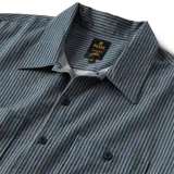 Camisa de manga corta a rayas verticales color azul con cuello clásico, cierre frontal con botones y dos bolsillos de parche en el pecho. Corte recto.