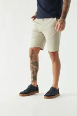 Bermuda color beige, de corte chino clásico, con bolsillos laterales y traseros, cierre con botón y cremallera, presillas para cinturón y logo bordado. Confeccionada en algodón y spandex.