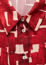 Vestido camisero midi con estampado abstracto en tonos rojo y beige, cuello camisero, manga larga y lazo ajustable en la cintura.