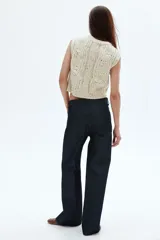 Chaleco corto de punto grueso color crema con textura tweed (neps oscuros), diseño sin mangas y escote en V con cierre frontal de botones marrones.