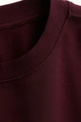 Buzo de tejido de punto color bordó, con cuello redondo y puños y bajo acanalados. Presenta un estampado frontal en blanco con el texto "RUNNING CLUB NEW YORK Central Park - Manhattan".