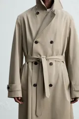 Trench largo regular fit color beige confeccionado en tejido italiano repelente al agua. Tiene cuello con solapas de pico, manga larga con puño ajustable con trabilla, bolsillos de vivo en cadera, bolsillo interior, cinturón del mismo tejido en cintura, bajo con abertura en centro espalda y cierre frontal de botonadura cruzada.