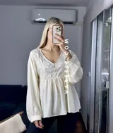 Blusa color crema con escote en V, mangas largas abullonadas con puños elásticos y detalles de encaje y bordado en el frente.