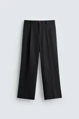 Pantalón de vestir negro, corte amplio, con pliegues en la cintura, bolsillos laterales y traseros de ojal.