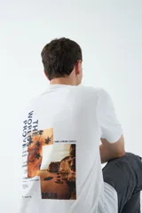 Remera blanca de algodón con estampado en la espalda con imágenes de paisajes y texto.
