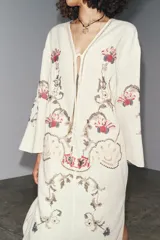 Vestido midi color crudo con bordados florales multicolores, escote en pico con lazos y mangas tres cuartos. Confeccionado en mezcla de algodón y lino.