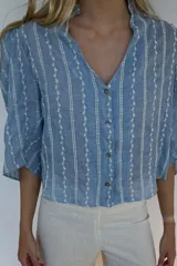 Blusa celeste de algodón liviano con bordado vertical de hojas blancas, manga 3/4, cuello mao con volados y cierre frontal con botones.