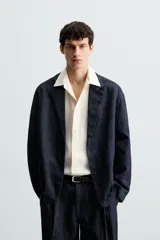 Blazer azul oscuro de denim, corte relaxed fit, con cuello de solapas de muesca, manga larga con puños abotonados, bolsillos de solapa en la cadera, abertura en el centro de la espalda y cierre frontal con botones.