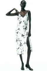 Vestido largo blanco con estampado de flores negras, escote pico y tirantes finos con ribete negro.