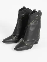 Botas de caña media de cuero vegano color negro con puntera fina y detalles de tachas doradas. El diseño incluye una solapa superpuesta en el empeine y un pequeño tacón cuadrado.