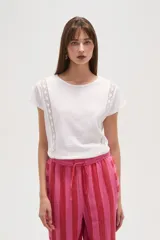 Remera blanca de algodón con apliques de encaje en los hombros, corte holgado y cuello redondo.