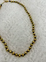 Collar corto de perlas doradas con hilo de seda azul marino y cierre de mosquetón dorado con cadena de extensión.