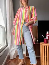 Vestido camisero largo con estampado de rayas verticales en tonos rosa, naranja, verde y blanco. Tiene cuello mao, mangas 3/4 con puños y cierre frontal con botones.