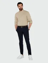 Camisa de vestir color beige claro, de corte clásico, con cuello abotonado y mangas largas.
