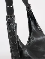 Cartera hobo color crudo de cuero sintético, con correa de hombro ajustable y múltiples cierres decorativos en el frente.