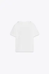 Camiseta blanca de corte recto, cuello redondo y mangas cortas. Presenta un lazo negro estampado en el frente.