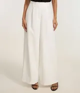 Pantalón pantalona de corte sastrero color blanco, confeccionado en poliéster y elastano, con cintura ancha con trabillas y pliegues delanteros.