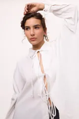 Camisa blanca de lino y algodón, con cuello clásico, cierre frontal con lazos y mangas largas abullonadas con puños ajustables con lazos.