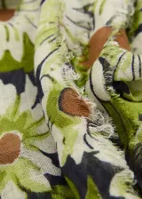 Fular rectangular de tejido mezcla de lino con estampado de flores en tonos verde, blanco y marrón sobre fondo negro.