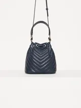 Cartera tipo bucket azul marino con diseño matelaseado en forma de chevron. Tiene doble asa, una corta superior y otra larga regulable para usar al hombro o cruzada. El cierre es con cordón ajustable.