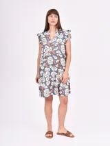 Vestido corto negro con estampado floral en blanco y naranja. Presenta cuello en V con abertura y botones, y mangas cortas con volados.