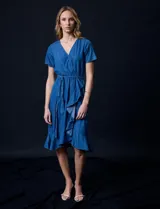 Vestido de tencel azul con escote en V cruzado, cintura elastizada con lazo, manga corta con volados y falda midi con volados.