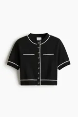 Saco corto negro en tejido de punto tupido con ribetes blancos en cuello, mangas y ruedo. Tiene cuello redondo, botones metálicos al frente y bolsillos superiores decorativos.