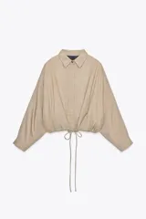 Chaqueta bomber color beige con cuello solapa y manga larga. Tiene bolsillos delanteros y bajo ajustable con cordones. Cierre frontal con botones ocultos.