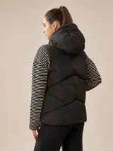 Chaleco puffer color borgoña con capucha, cierre frontal con botones a presión y bolsillos laterales. Diseño acolchado y corte recto.