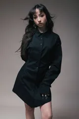 Vestido corto negro estilo camisero con botones frontales, mangas largas y lazos laterales ajustables.