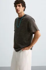 Camiseta de hombre de corte relaxed fit, con cuello redondo y mangas cortas. Diseño a rayas horizontales en tonos negro y dorado.