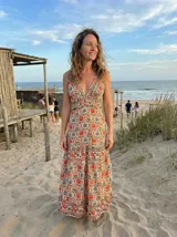 Vestido largo estampado con escote profundo en V y tirantes finos. El estampado presenta motivos florales en tonos terracota, azul apagado y crema, dispuestos en un patrón repetitivo con franjas decorativas.