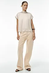 Blusa color crudo de tejido satinado, con cuello subido, manga sisa y cierre en la espalda con lazada y botones.