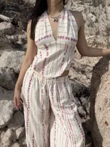 Pantalón ancho de tiro alto, color crema con estampado vertical de líneas irregulares en tono rosado/malva. Presenta cintura elástica.