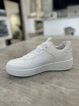 Zapatillas urbanas blancas de cuero sintético con cordones y suela de goma.