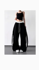 Pantalón deportivo negro de corte ancho con cintura elástica blanca con cordón y dos líneas verticales blancas a los costados.