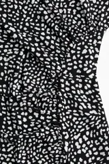 Vestido midi negro con estampado de manchas blancas, sin mangas, de punto elástico, corte ajustado, cuello alto y costura curva fruncida en un lateral para conseguir un efecto drapeado que realza la figura.