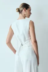 Chaleco blanco con escote en V, corte entallado, botones forrados y hebilla ajustable en la espalda.