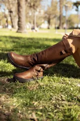 Bota de cuero color chocolate, de caña alta, con suela track y detalle de tira en la parte superior.