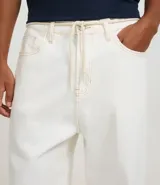 Pantalón de corte skater confeccionado en sarga de algodón color crudo, con cintura con trabillas, cordón ajustable, cierre tradicional, bolsillos y costuras contrastantes.