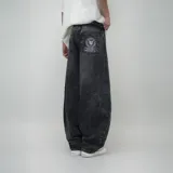 Pantalón de jean negro con lavado oscuro y efecto desgastado, de corte ultra ancho y tiro alto. Presenta un parche circular con logo en el bolsillo trasero derecho.