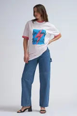 Camiseta blanca de corte holgado con estampado frontal que incluye un cuadrado azul con bordes negros y la frase "Be real Not Perfect" en letras negras con un rayo rosa que atraviesa el estampado.