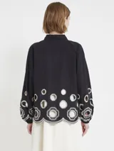 Camisa negra amplia con botones en el frente, mangas abullonadas sobre el puño y apliques de macramé en la parte baja, tanto en el frente como en la espalda y las mangas.