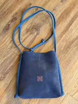 Cartera tipo bandolera azul de cuero gamuzado, con correa larga trenzada y logo bordado en color salmón.