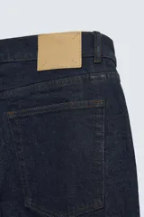 Jeans de corte slim fit confeccionados en denim de algodón sin lavados, color azul oscuro. Cierre frontal con botones y cinco bolsillos.