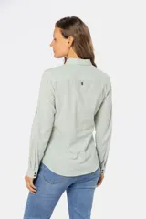 Camisa color beige de lino, de manga larga con botones metálicos personalizados y presilla en la manga. Tiene cuello clásico, cierre frontal parcial con botones y bolsillo de parche en el pecho.