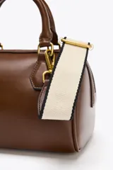 Bolso marrón formato city con asa doble de mano con detalles metálicos y correa interior extraíble en tejido canvas con posición bandolera. Bolsillo interior con cierre mediante cremallera metálica.
