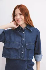 Camisa de denim azul con cuello clásico, cierre frontal con botones blancos, mangas largas con puños abotonados y dos bolsillos cargo con solapa en el pecho.